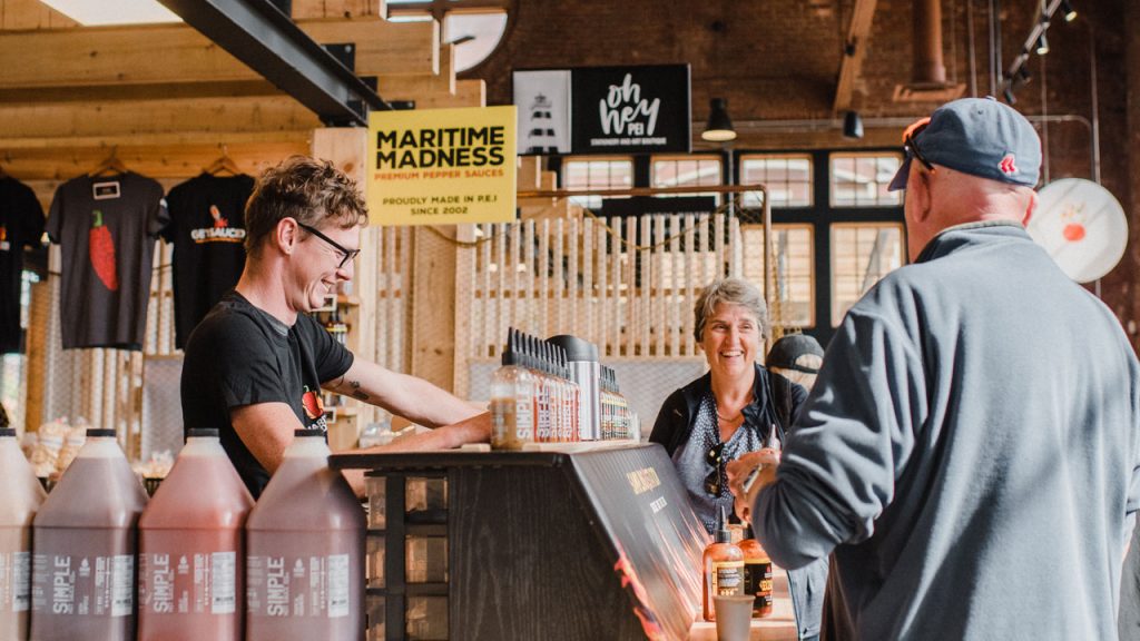 Customer enjoying samples at Maritime Madness hot sauce counter in Founders’ Food Hall & Market, Charlottetown PEI