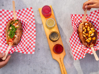 Lobster & Poutine Baked Potatoes with Assorted Flight | Founders’ Food Hall & Market Gourmet baked potatoes topped with lobster and poutine served on red checkered paper with a cider flight at Founders’ Food Hall & Market.