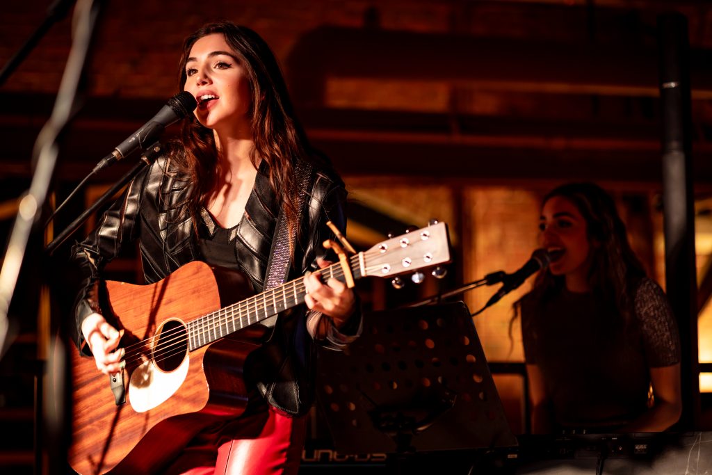 Live Music at Founders’ Food Hall & Market | Charlottetown Entertainment Female musician performing live at Founders’ Food Hall & Market, singing and playing guitar on stage.