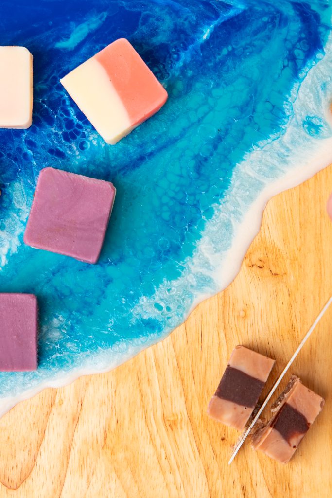 Handmade Fudge Squares from Oh Fudge PEI Assorted handmade fudge squares displayed on a wooden and resin ocean serving board with vibrant blue waves.