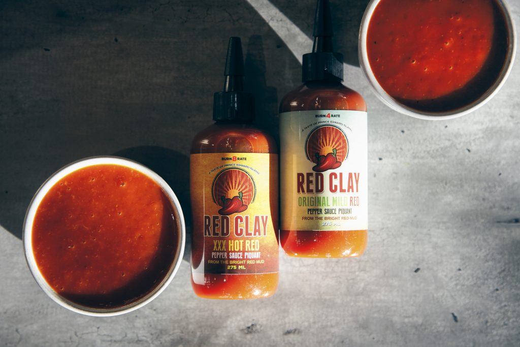Bottles of Red Clay hot sauce with bowls of rich red pepper sauce