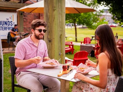 Couple enjoying food on the best patio Charlottetown at Founders’ Food Hall & Market with live music in the background.
