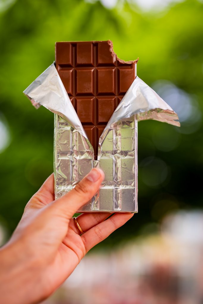 Hand holding a bitten chocolate bar wrapped in foil outdoors
