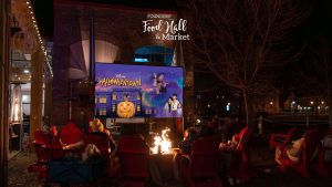 Outdoor movie night at Founders’ Food Hall & Market in Charlottetown showing Halloweentown, with families gathered around fire pits in red chairs under string lights.
