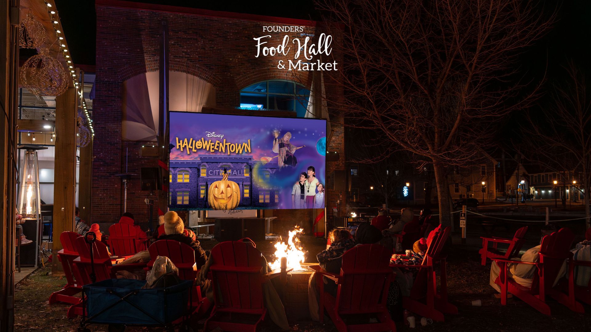 Outdoor movie night at Founders’ Food Hall & Market in Charlottetown showing Halloweentown, with families gathered around fire pits in red chairs under string lights.