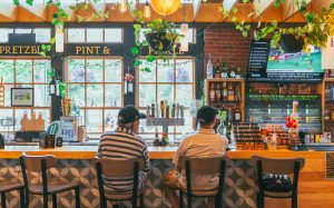 Two guests sitting at the Pretzel, Pint & Pickle bar in Charlottetown with Island craft beer taps and bottles on display