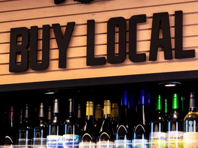 “Buy Local” sign with PEI map above shelves of wine bottles at Notables inside Founders Food Hall & Market in Charlottetown.
