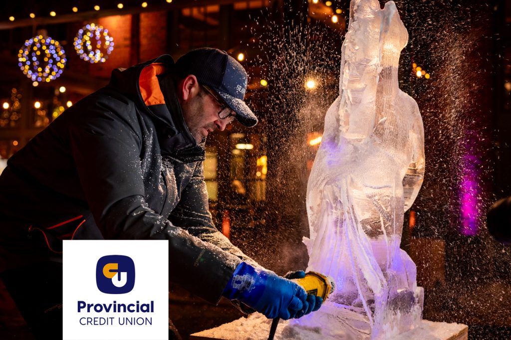 Ice sculptor using tools to carve a detailed ice sculpture at a winter event with Provincial Credit Union branding