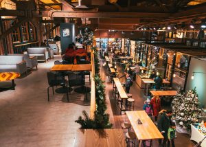 People walking through a decorated indoor market hall with Christmas trees, lights, and wooden dining tables