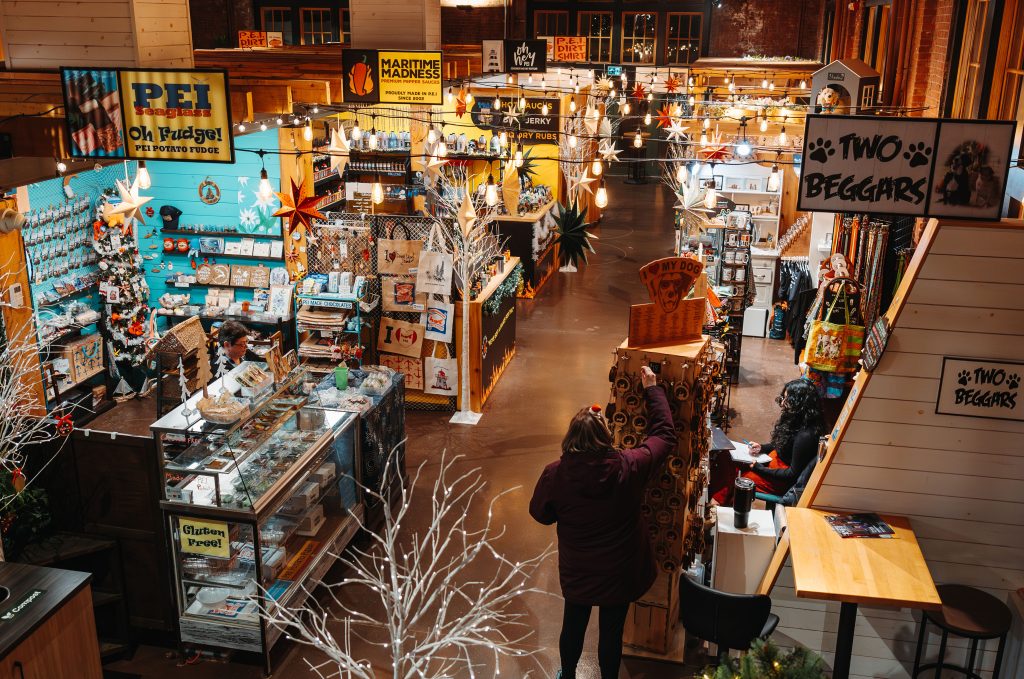 Shoppers exploring an indoor artisan market with PEI-made products, handcrafted goods, and festive holiday decorations