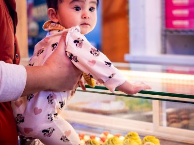 Father holds baby while they look at colorful pastries in a bakery display case.