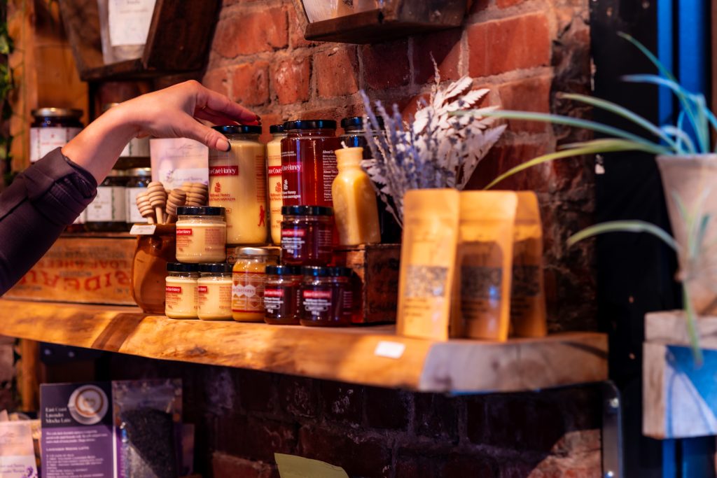 Hand reaching for jars of local PEI honey, spreads, and pantry goods on a rustic shelf at Founders Food Hall in Charlottetown.