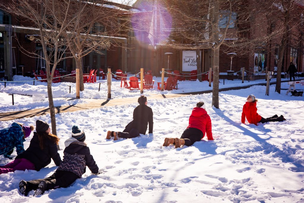 People participating in outdoor winter wellness activities in the snow at Founders Food Hall Green Space in Charlottetown PEI