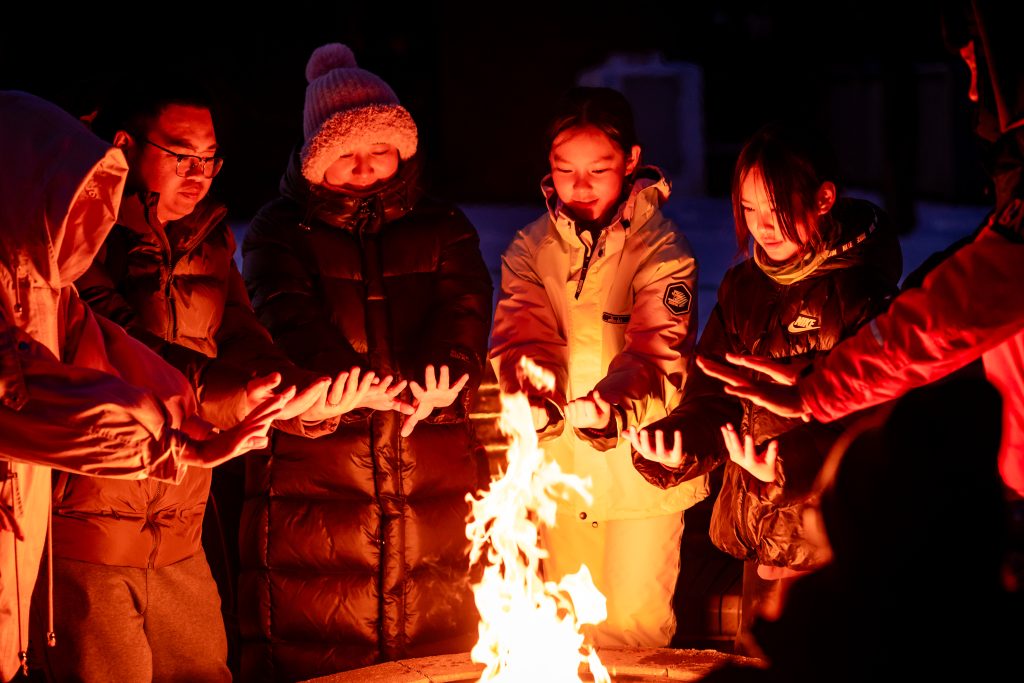 Family warming hands by outdoor fire pit at Founders Food Hall & Market during winter in Charlottetown PEI